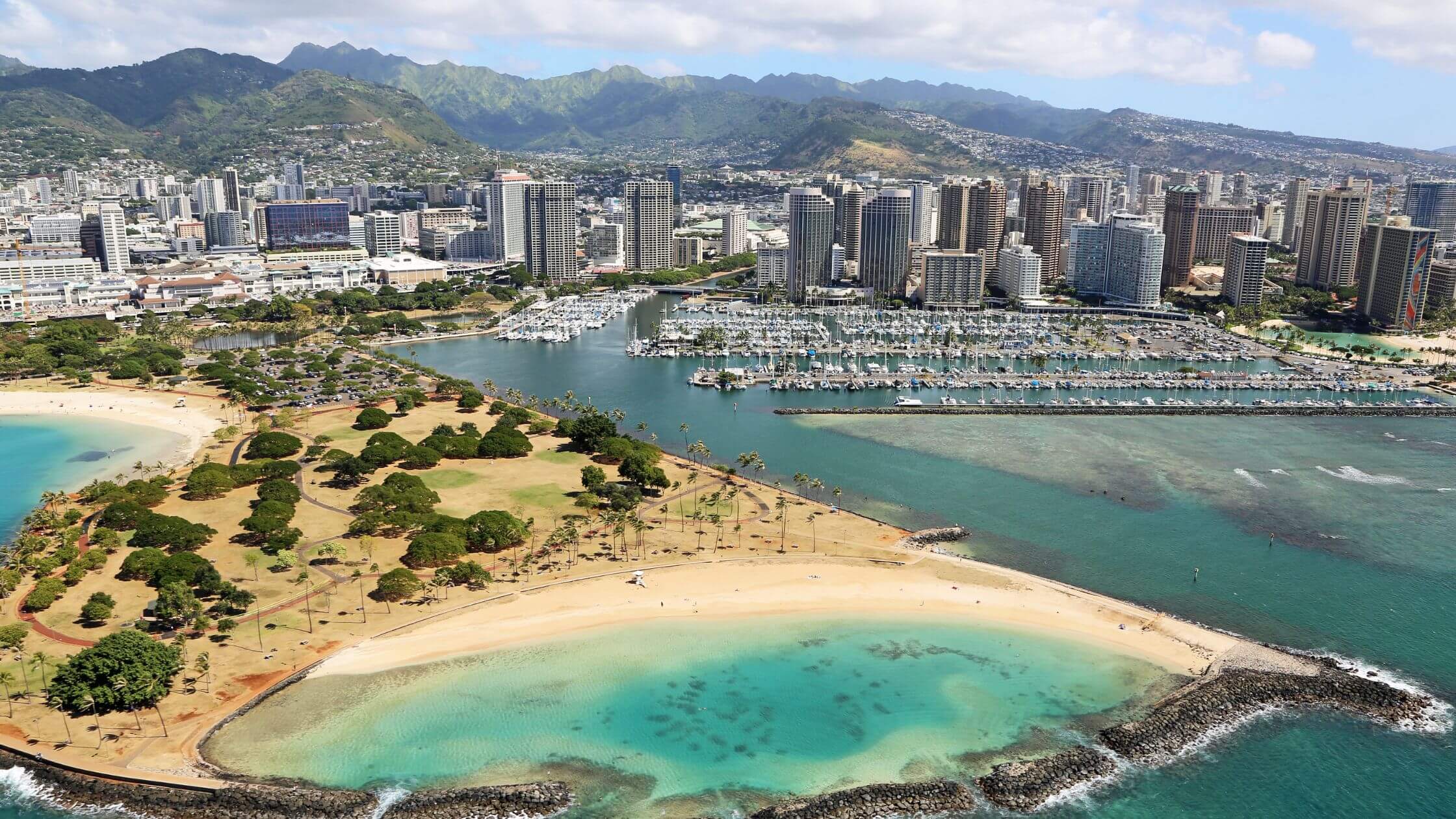 Aerial drone view of Ala Moana Beach Park, the Magic Island lagoon, and the Honolulu skyline along the southern shore of Oahu, Hawaii.